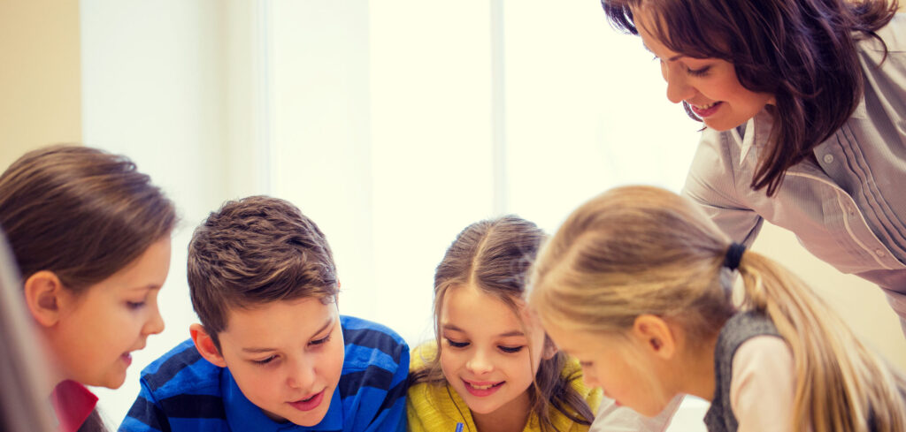 education, elementary school, learning and people concept - teacher helping school kids writing test in classroom